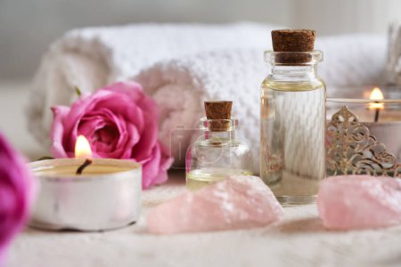 Two bottles of aromatherapy essential oil with rose de Mai flowers, rose quartz stones and white spa towels