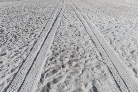 Téléchargez les photos : Fond de sable de plage doux avec des traces de pneus de VTT menant au loin, espace de copie créatif pour les thèmes de voyage, de loisirs et de voyage, aspect horizontal - en image libre de droit
