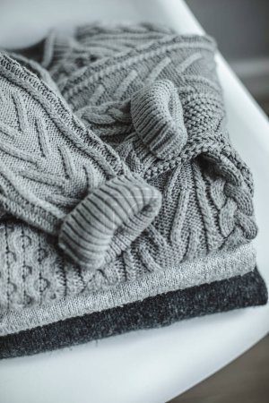 Photo for Stack of gray knitted warm cozy sweater on white chair. Autumn or Winter concept. Top view. - Royalty Free Image