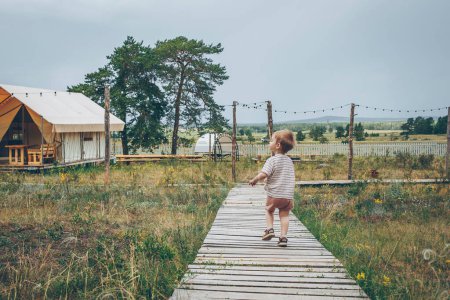 Foto de Niño de 2-3 años corriendo por un sendero de madera en un camping. Camping y vacaciones concepto al aire libre - Imagen libre de derechos