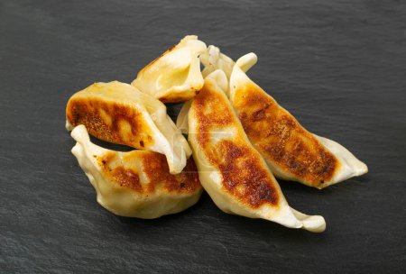 Dumplings chinos de Gyoza, Jiaozi de verduras fritas, pila Momo de pollo, Grupo de Gyoza asiática sobre fondo de placa de piedra negra