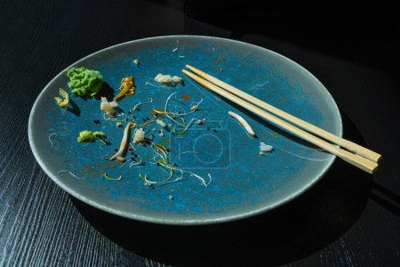 Foto de Placa de sushi sucia en la mesa negra, cuenco vacío después de la cena de sushi, almuerzo asiático terminado, ensalada y salsa Wasabi en el fondo de la placa azul Vista superior - Imagen libre de derechos