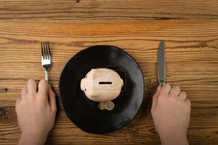 Foto de Piggy Bank on Plate, Eat Up Eating Savings, Financial Difficulties Concept, Saving Pig as Food, Eating Home Finances, Piggy Bank on Plate Top View - Imagen libre de derechos
