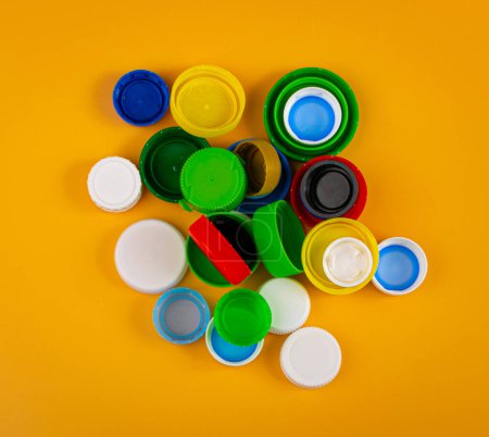 Téléchargez les photos : Bouchons de bouteille en plastique Pile. Groupe de matériaux HDPE de recyclage, Couvercle en polyéthylène, Groupe de capsules colorées sur fond jaune - en image libre de droit
