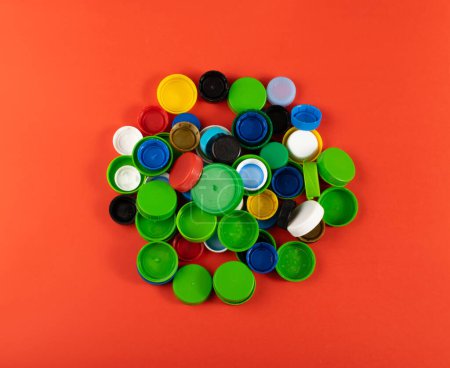 Téléchargez les photos : Bouchons de bouteille en plastique Pile. Groupe de matériaux HDPE de recyclage, Couvercle en polyéthylène, Groupe de capsules colorées sur fond rouge - en image libre de droit