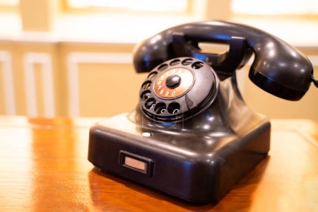 Photo for Antique black telephone on wooden table, blurred natural light background. - Royalty Free Image