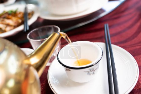 Gießen Sie natürlichen Kamillentee aus der Teekanne in die Tasse auf dem Geschirr.
