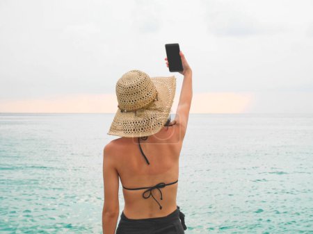 Photo for Woman with sunburned back taking a selfie on the beach - Royalty Free Image