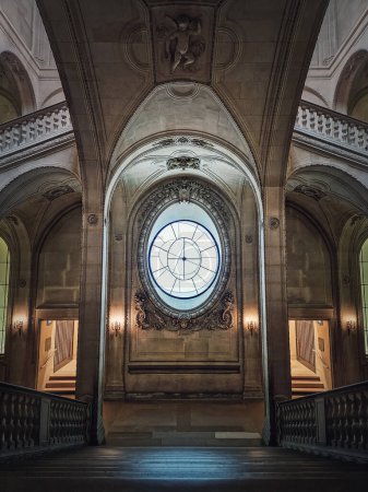 Foto de Palacio del Louvre detalles arquitectónicos simétricos de una sala con escalera de piedra, barandillas adornadas, diferentes pasillos y una ventana tipo reloj en el centro, París, Francia - Imagen libre de derechos