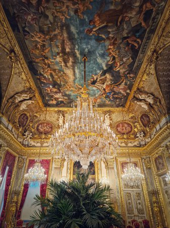 Foto de Hermosos apartamentos Napoleón decorados en el palacio del Louvre. Habitaciones familiares reales con cortinas rojas cardinales, paredes doradas adornadas, pinturas y lámparas de araña de cristal suspendidas del techo - Imagen libre de derechos