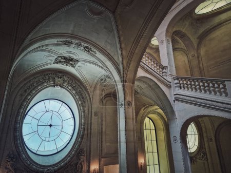 Foto de Palacio del Louvre detalles arquitectónicos de una sala con escaleras de piedra, barandillas adornadas y ventanas redondas, París, Francia - Imagen libre de derechos
