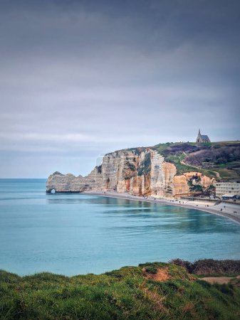 Photo for Idyllic view to Etretat coastline with the famous Notre-Dame de la Garde chapel on the Amont cliff. Shore washed by Atlantic ocean waters, Normandy, France - Royalty Free Image