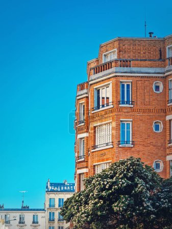 Photo for Beautiful orange brick building with a blooming tree at the bottom under a clear blue sky background in Asnieres-sur-seine a suburb of Paris, France - Royalty Free Image