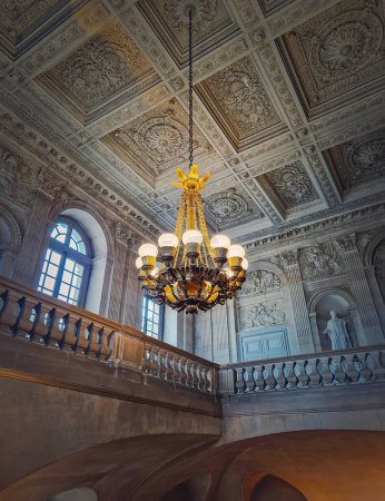 Téléchargez les photos : Détails architecturaux d'une salle d'escalier ornée d'un lustre vintage lumineux suspendu au plafond du château de Versailles, France - en image libre de droit
