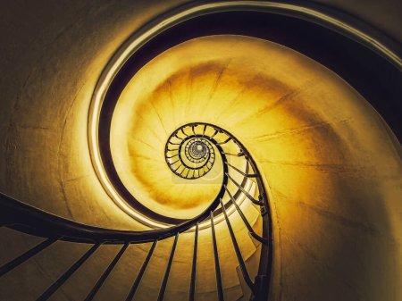 Téléchargez les photos : Escalier en spirale abstrait tourbillonnant perspective hypnotisante. Vue en bas des escaliers circulaires à débordement lumineux en fond de lumière jaune - en image libre de droit