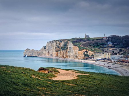 Photo for Sightseeing view to Etretat coastline with the famous Notre-Dame de la Garde chapel on the Amont cliff. Seashore washed by Atlantic ocean waters, Normandy, France - Royalty Free Image