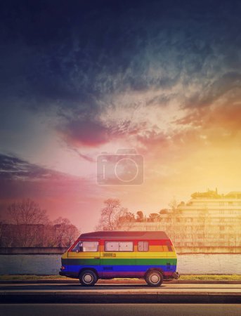 Téléchargez les photos : Fourgon vintage peint arc-en-ciel garé sur le bord de la rue dans le fond de lumière du coucher du soleil. Couleurs Lgbtq, bus symbole de fierté - en image libre de droit