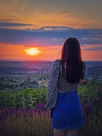 Téléchargez les photos : Vue arrière d'une femme en jupe regardant le coucher du soleil sur la vallée. Été naturel crépuscule scène - en image libre de droit