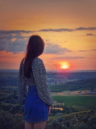 Téléchargez les photos : Vue arrière d'une fille regardant le coucher du soleil depuis le sommet de la vallée. Scène naturelle du soir d'été - en image libre de droit