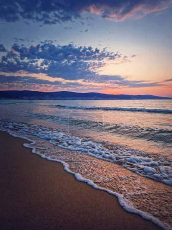 Téléchargez les photos : Lever de soleil à la mer avec des vagues mousseuses sur le sable et un ciel coloré à l'horizon. Été et fond de voyage, Sunny Beach littoral en Bulgarie - en image libre de droit