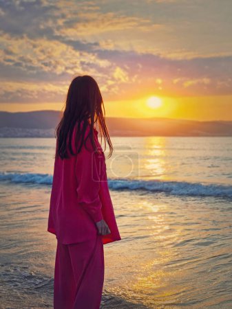 Foto de Estética joven mujer vista trasera viendo el amanecer por encima de las colinas en el mar. Hermosa escena del amanecer, vacaciones de verano fondo - Imagen libre de derechos