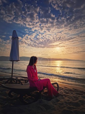 Photo for Woman relaxing on the sunbed as meets the dawn at the beach. Beautiful sea sunrise scene, summer vacation seaside, travel and holiday relaxation concept - Royalty Free Image