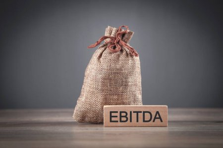 Money bag with a text EBITDA on wooden block.