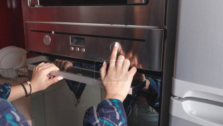Téléchargez les photos : Doigt féminin touchant le bouton du four électrique dans la cuisine. - en image libre de droit