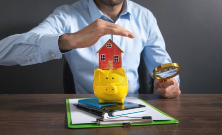 Businessman protect piggy bank with a house model.