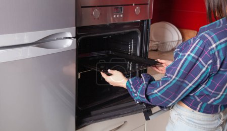 Téléchargez les photos : Femme utilisant four électrique dans la cuisine. - en image libre de droit