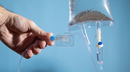 Foto de Mano masculina comprobando un goteo intravenoso en el fondo azul. - Imagen libre de derechos