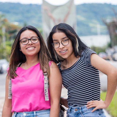 best friends posing on camera, latin-american girls wearing glasses and smile 