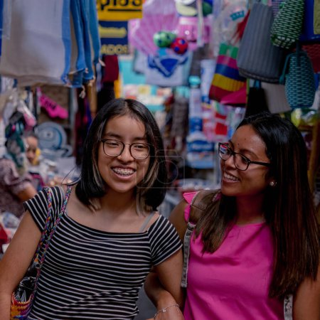 Téléchargez les photos : Meilleurs amis faisant du shopping en ville, les étudiants latino-américains sourient tout en marchant dans le marché de vêtements de rue - en image libre de droit