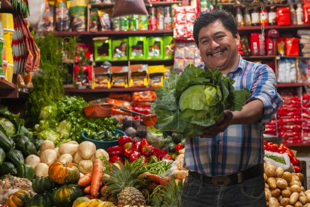 Photo for Food bazaar in Guatemala, happy latin-american man selling vegetables and fruits, man showing lettuce salad - Royalty Free Image