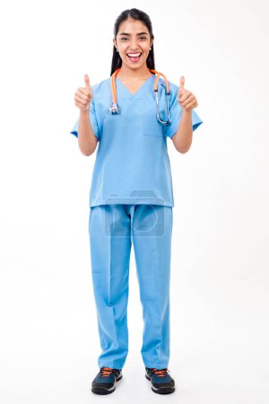 Téléchargez les photos : Young female doctor standing on white background and showing thumbs up - en image libre de droit