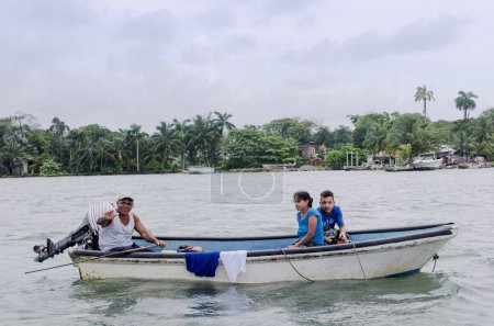 Téléchargez les photos : GUATEMALA, RIO DULCE IZABAL - MARS 2017 : Pêcheur nageant sur un bateau en famille, fond de forêt tropicale - en image libre de droit