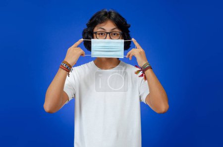 Foto de Adolescentes se ponen máscaras médicas con camisas blancas y pulseras típicas sobre fondo azul - Imagen libre de derechos