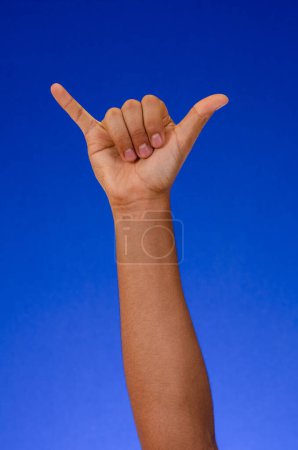 Foto de Arm raised making symbol or fingers signal, on a blue background - Imagen libre de derechos