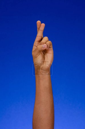 Foto de Fingers crossed as a symbol of luck. arms and palms making signs on a blue background - Imagen libre de derechos