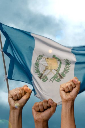 Foto de People holding fists on background of waving Guatemalan flag and cloudy sky - Imagen libre de derechos