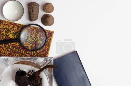 smoking pipe with tobacco, magnifying glass and old mayan relicts  on white background
