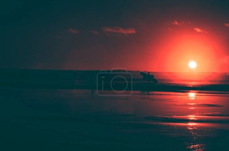 Téléchargez les photos : Coucher de soleil lumineux rouge et surfeur avec planche dans l'océan - en image libre de droit