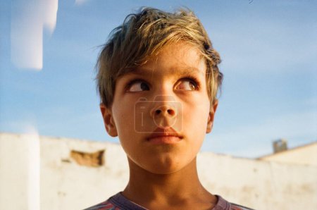 Foto de Retrato de niño mirando hacia otro lado, rayos de sol y cielo azul en el fondo - Imagen libre de derechos