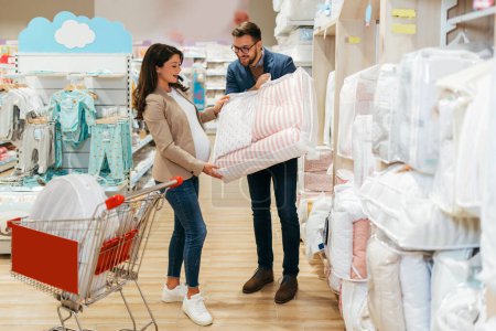 Photo for Attractive middle age couple enjoying in buying clothes and bed sheets for their new baby. Heterosexual couple in baby shop or store. Expecting baby concept. - Royalty Free Image