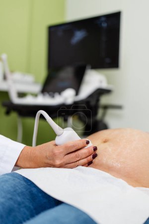 Doctora haciendo ecografía para una hermosa mujer embarazada. Vista lateral. Embarazo moderno y concepto sanitario.