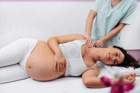 Téléchargez les photos : Belle jeune femme enceinte profiter et se détendre pendant un traitement de massage spécial pour maintenir une grossesse en bonne santé. - en image libre de droit