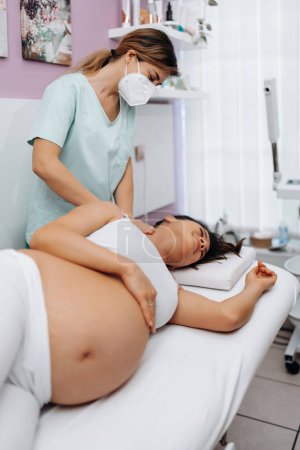 Téléchargez les photos : Belle jeune femme enceinte profiter et se détendre pendant un traitement de massage spécial pour maintenir une grossesse en bonne santé. - en image libre de droit