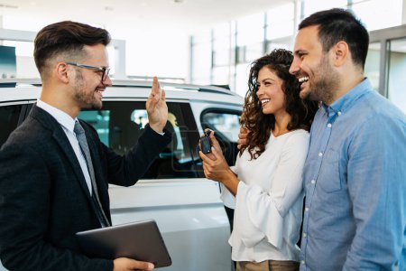 Middle age couple buys a car at a car dealership. The seller gives them the car keys. They are very happy.
