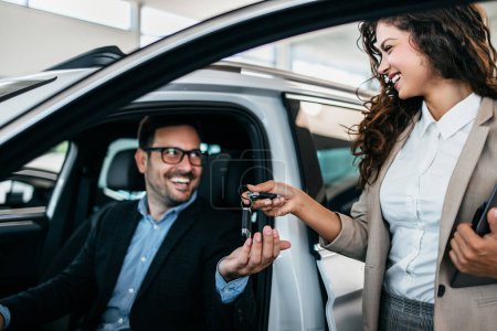 Photo for Happy middle age businessman buying new and expensive car. Beautiful female dealer helps him to make right decision. - Royalty Free Image
