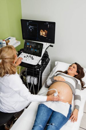Téléchargez les photos : Female doctor doing ultrasound scan for a beautiful pregnant woman. Side view. Modern pregnancy  and healthcare concept. - en image libre de droit